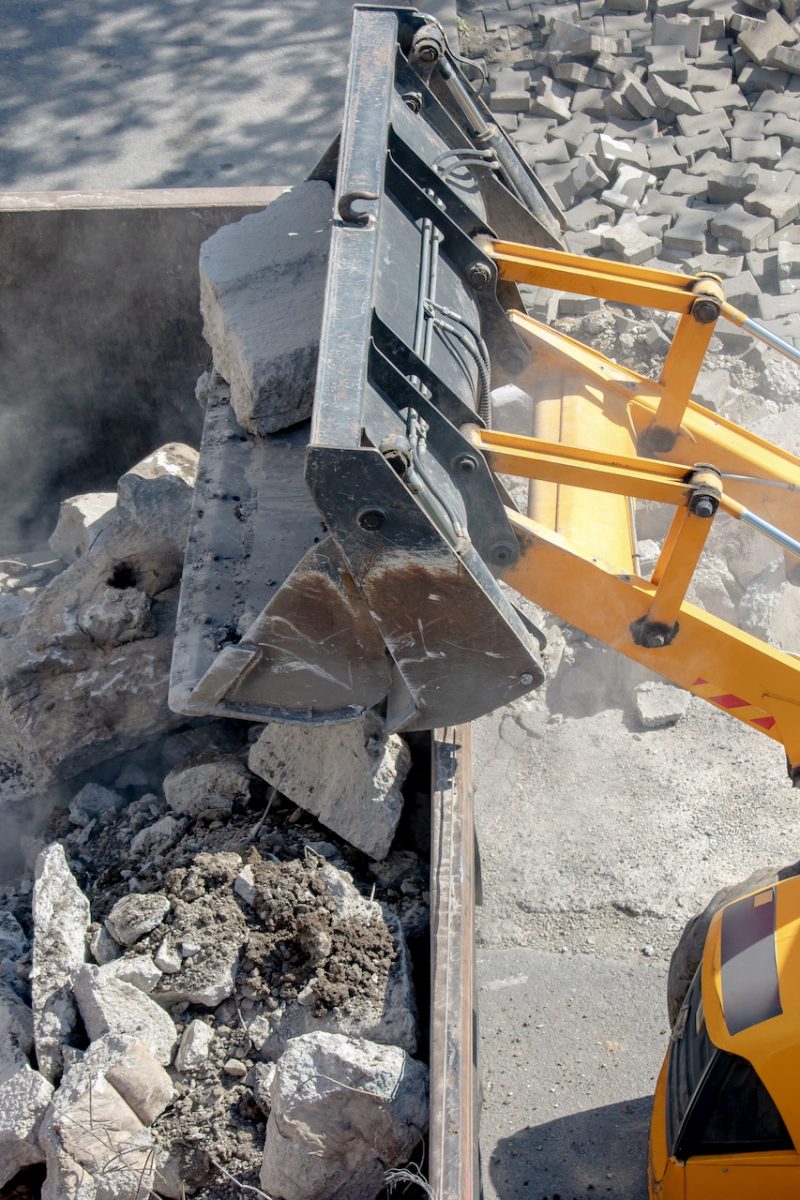 Bulldozer loader uploading concrete debris into dump truck at construction site